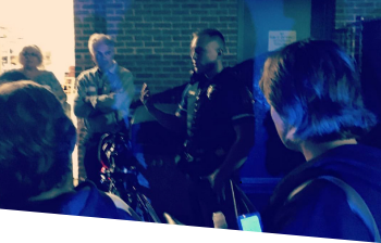 An officer giving a lecture at night outside with his motorcycle beside him