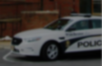 A faded image of a Winchester Police Department cruiser parked in front of a brick building