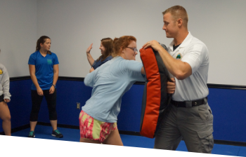 A teen girl practicing self defense with as an instructor holds a boxing/kick pad
